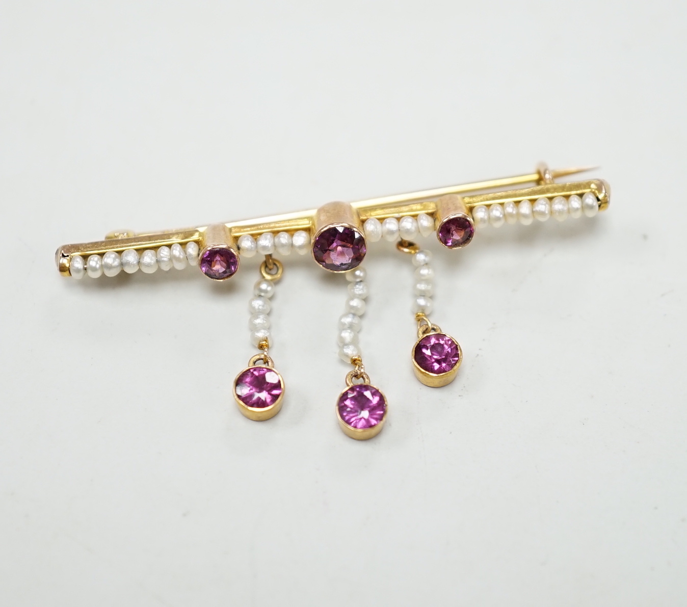 An early 20th century yellow metal, garnet and seed pearl cluster set drop bar brooch, 43mm, gross weight 2.1 grams.